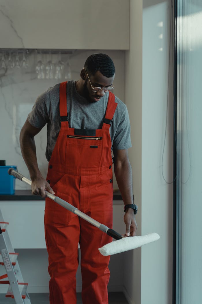 services-02 Man wearing red overalls using a mop indoors, depicting cleanliness and manual work.